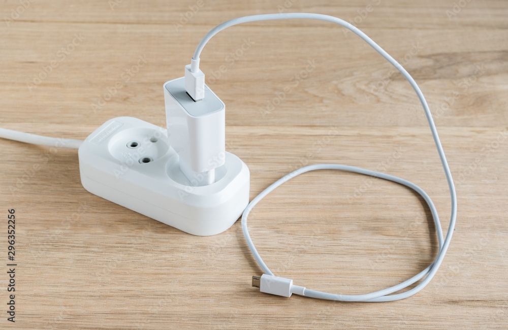 Charger with usb cable for smartphones connected to a power strip. Wood table background. Charger with usb cable for smartphones connected to a power strip. Wood table background.