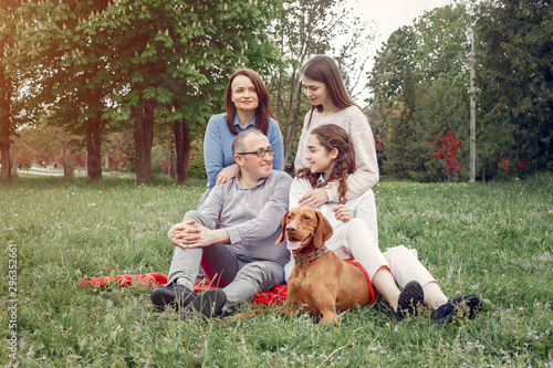 Family in a summer park. People sitting with a dog. Parents with a two daughters