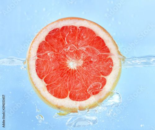 Falling of grapefruit piece into water on color background