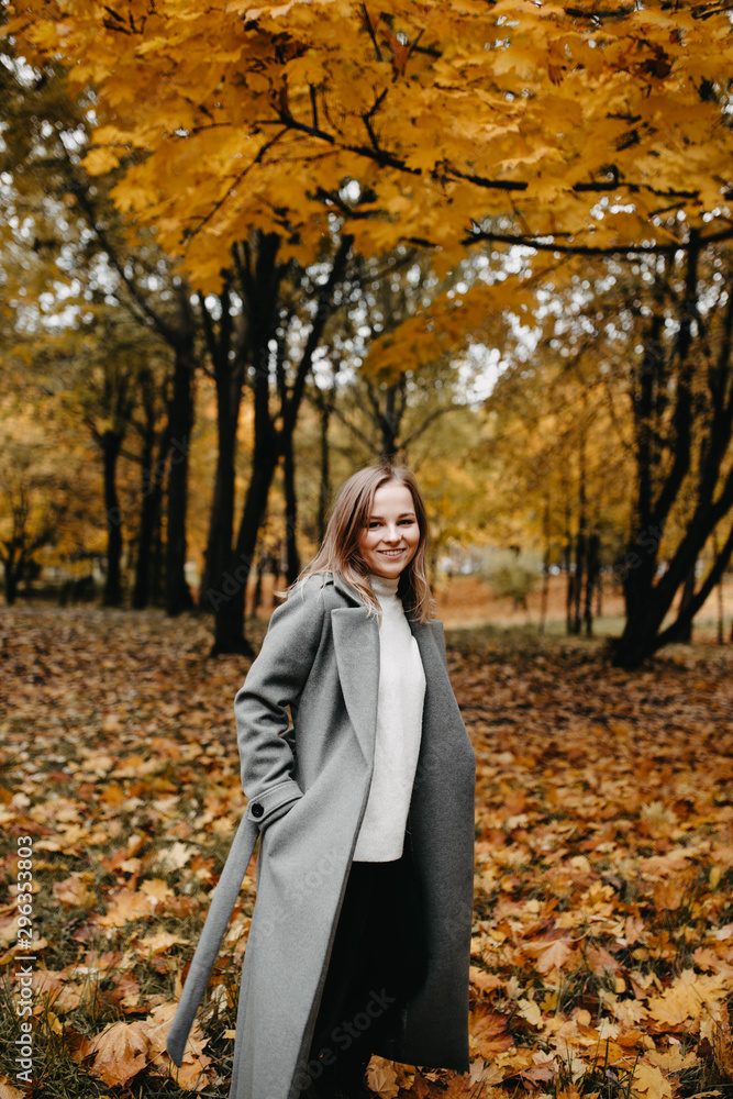 Autumn portrait of a young girl in an autumn park in a gray coat. Posing at a photo shoot in nature.