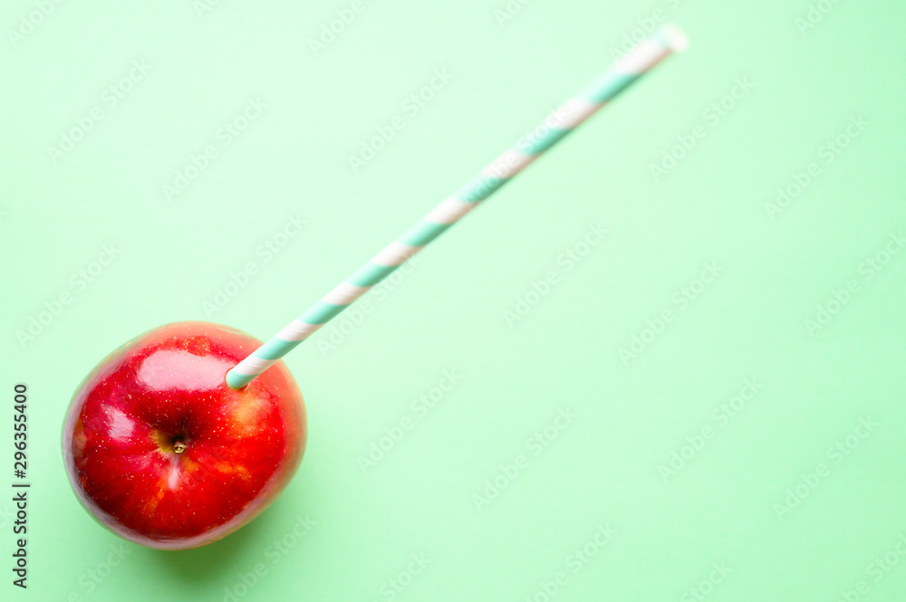 a ripe juicy bright red apple and in it a striped white and green paper drinking straw, located on a green background. space for text a ripe juicy bright red apple and in it a striped white and green paper drinking straw, located on a green background. space for text