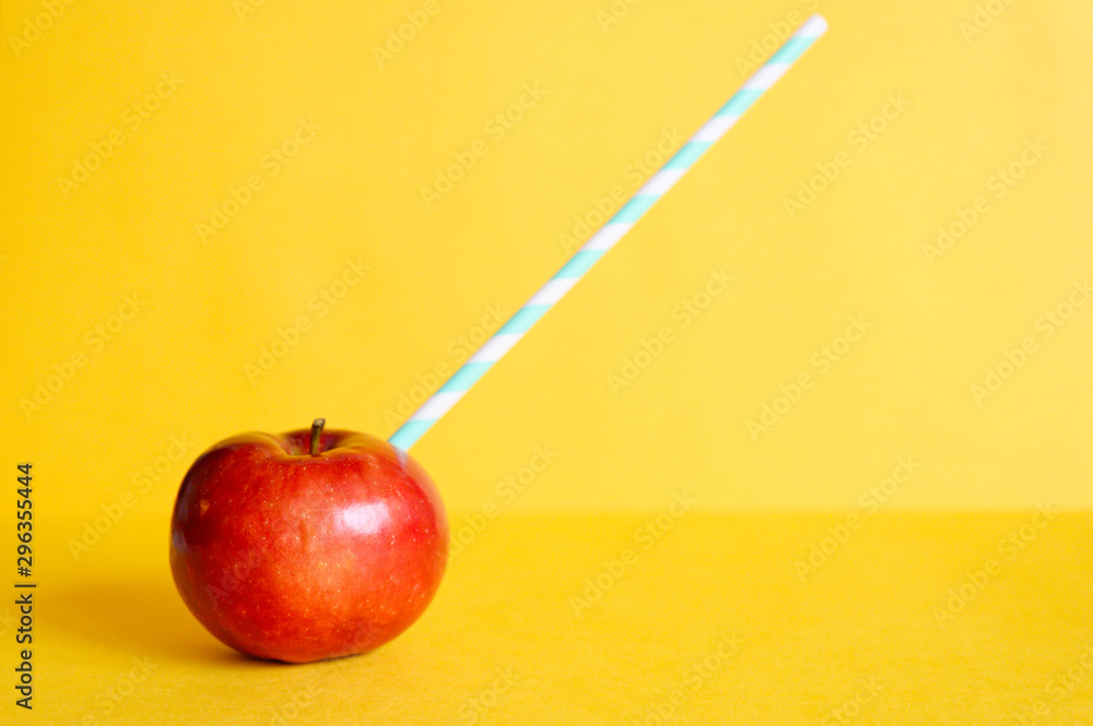 a ripe juicy bright red apple and in it a striped white and green paper drinking straw, located on a yellow background. space for text a ripe juicy bright red apple and in it a striped white and green paper drinking straw, located on a yellow background. space for text