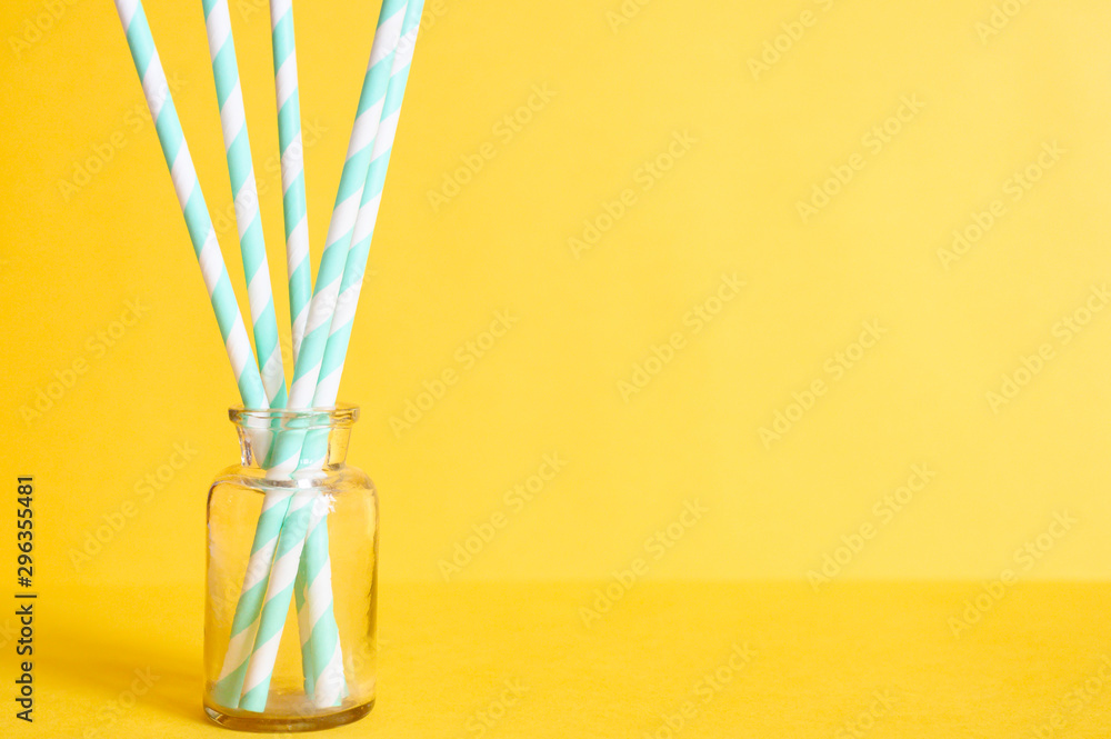 pile of paper striped white and green drinking straws for party in clear glass small bottle on yellow background