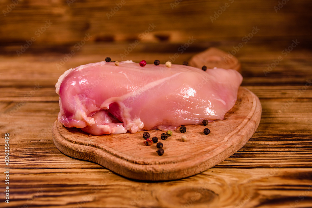 Cutting board with raw chicken fillet and different spices on wooden table