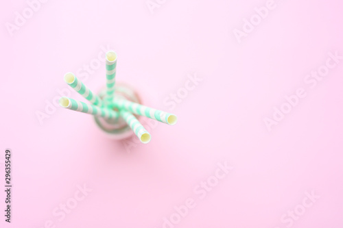 blurred pile of paper striped white and green drinking straws for party in clear glass small bottle on pink background. space for text