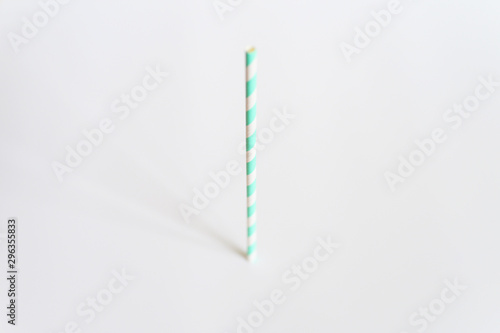 one paper striped white and green party drinking straw stands upright on a white background