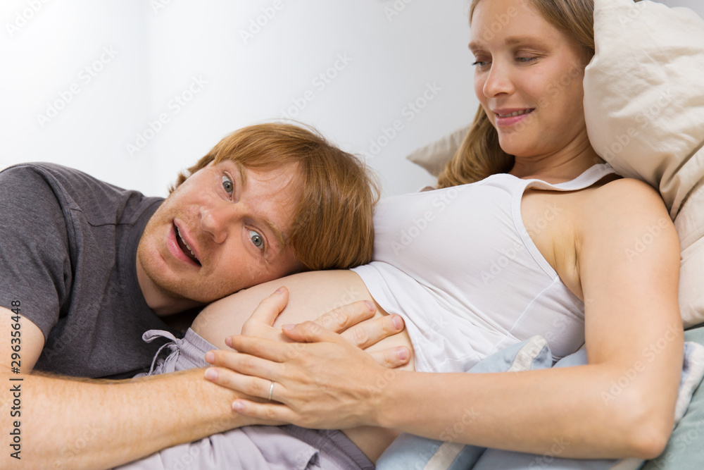 Excited expectant couple having fun at home. Happy future father listening to baby bump. Future parents concept Excited expectant couple having fun at home. Happy future father listening to baby bump. Future parents concept