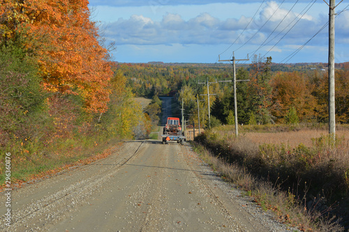 Farm tractor with hay wagon driving on a country road