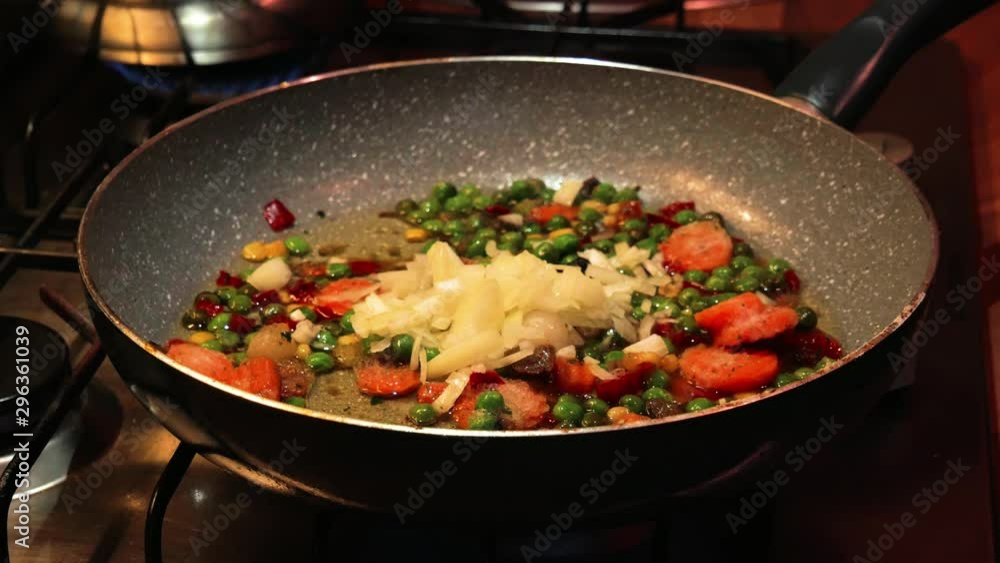 Pouring fresh chopped onions to a hot frying pan with vegetables in it. Pouring fresh chopped onions to a hot frying pan with vegetables in it.