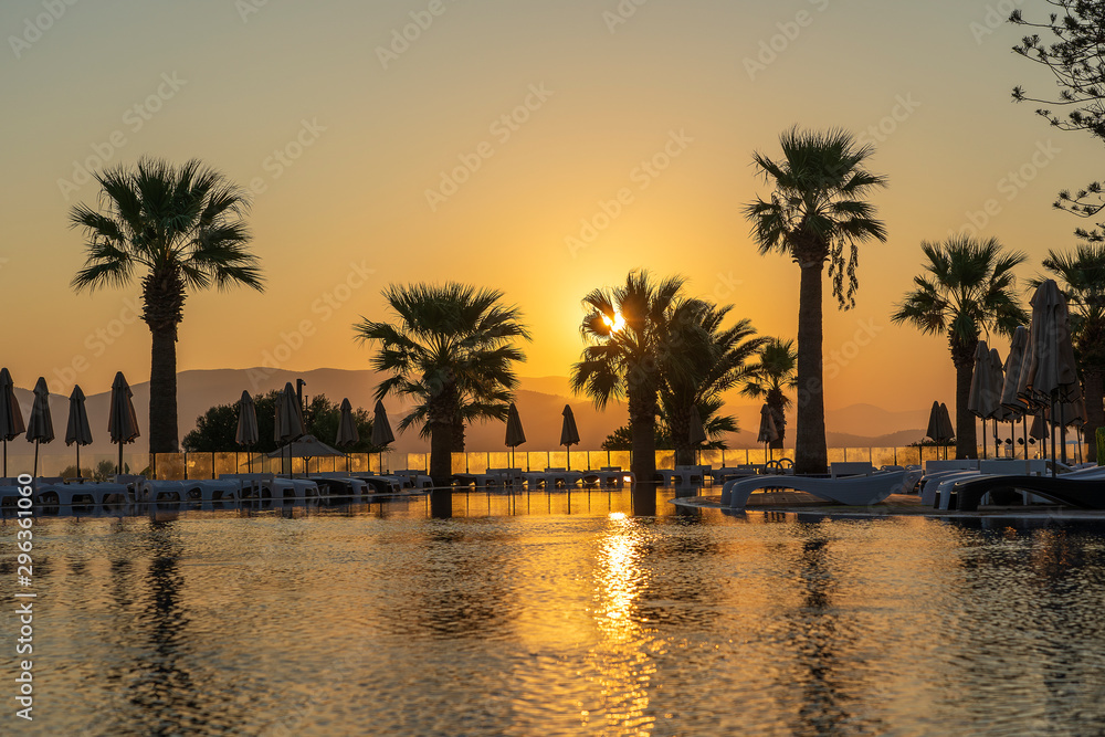 Obraz premium Magical sunrise with silhouette coconut palm tree and swimming pool in luxury hotel resort near sea. Beautiful morning seascape