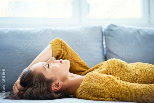 Cheerful young woman lying on sofa with eyes closed and relaxing photo