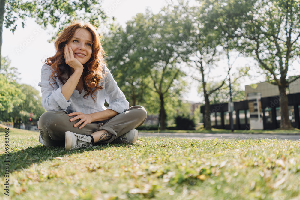 Smiling redheaded woman sitting on grass verge Smiling redheaded woman sitting on grass verge