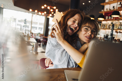 Two excited female, friends with laptop and credit card in a cafe photo