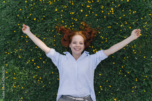 Portrait of happy redheaded woman lying on a flower meadow
