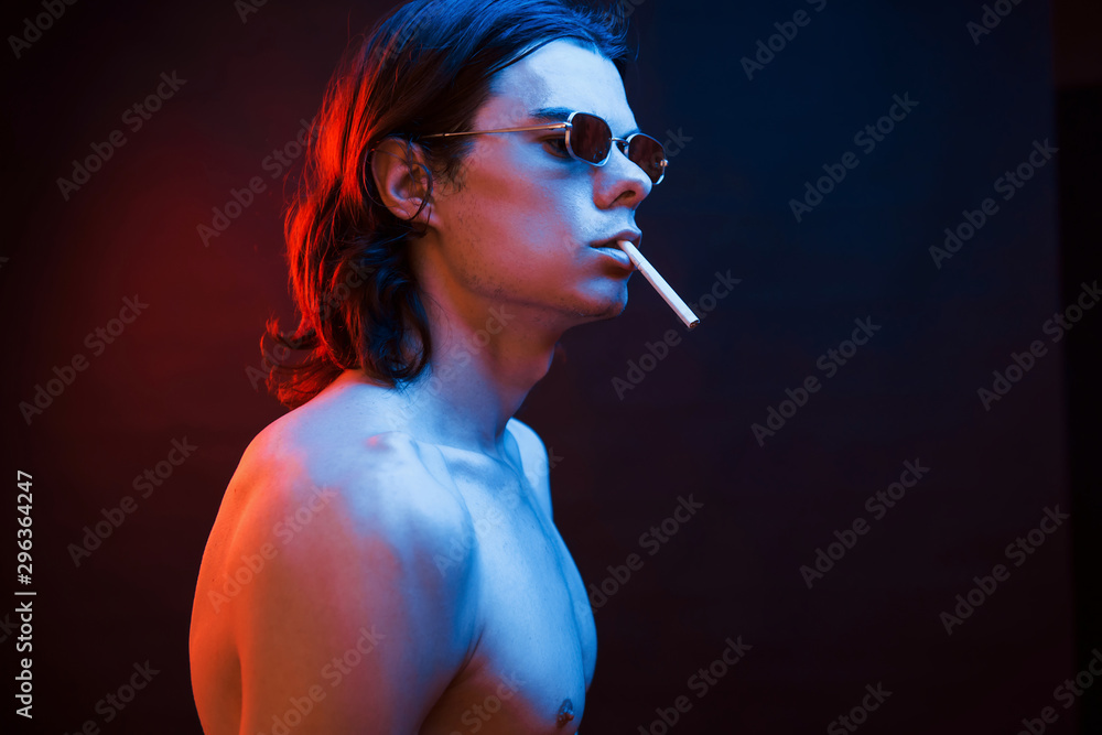 Fototapeta premium Smoking cigarette. Studio shot in dark studio with neon light. Portrait of serious man
