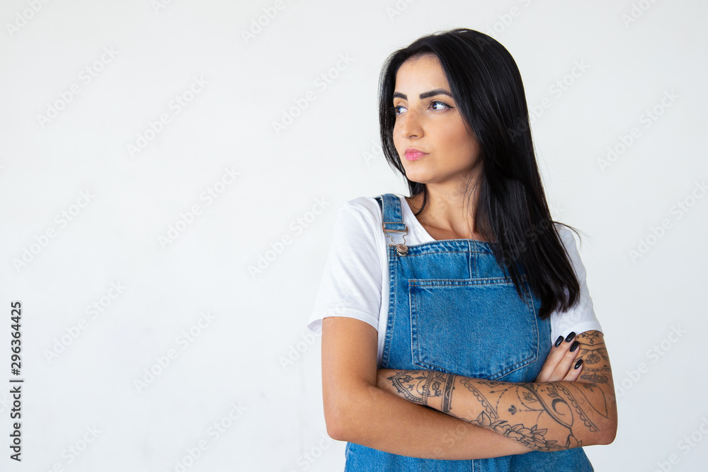 Serious young brunette with crossed arms looking aside. Thoughtful brunette lady posing on light background. Female beauty concept Serious young brunette with crossed arms looking aside. Thoughtful brunette lady posing on light background. Female beauty concept