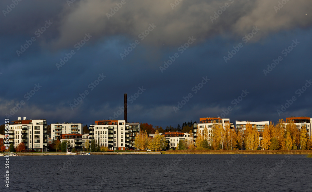 A city view with white apartment houses and yellow birches. Sky is dark blue with rain