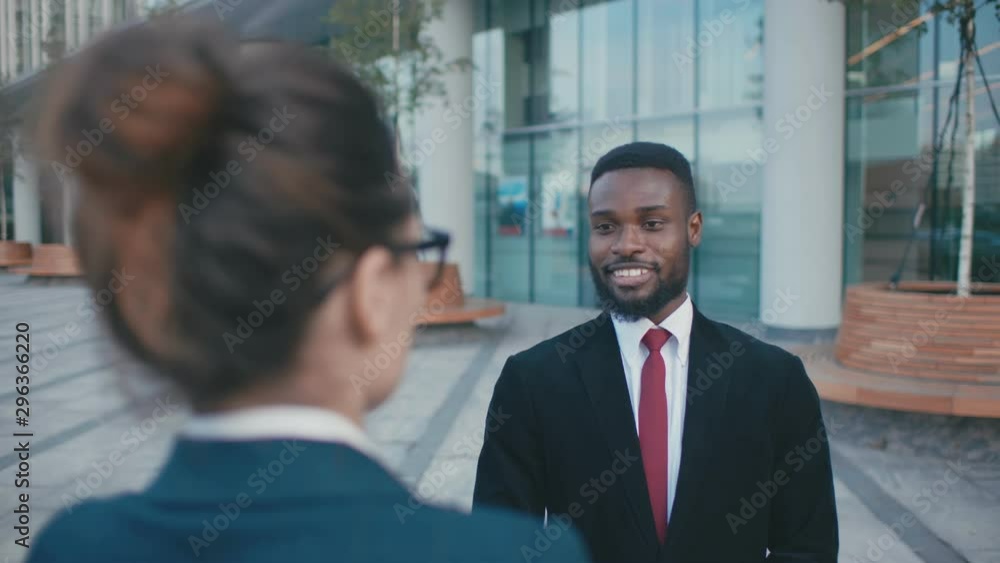 Male and female colleagues employees cooperating outdoor talking. Smiling black businessman and caucasian businesswoman discussing planning business project Male and female colleagues employees cooperating outdoor talking. Smiling black businessman and caucasian businesswoman discussing planning business project