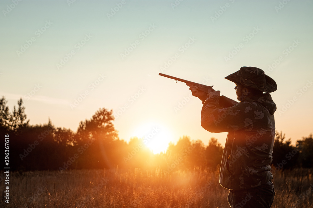Silhouette of a hunter in a cowboy hat with a gun in his hands on a background of a beautiful sunset. The hunting period, the fall season is open, the search for prey. Silhouette of a hunter in a cowboy hat with a gun in his hands on a background of a beautiful sunset. The hunting period, the fall season is open, the search for prey.