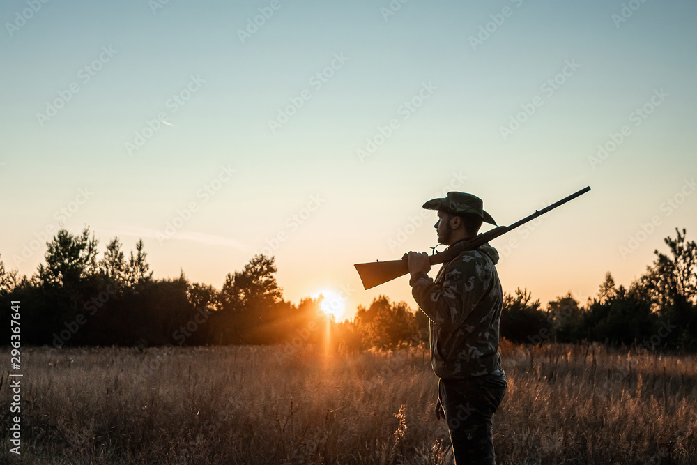 Silhouette of a hunter in a cowboy hat with a gun in his hands on a background of a beautiful sunset. The hunting period, the fall season is open, the search for prey. Silhouette of a hunter in a cowboy hat with a gun in his hands on a background of a beautiful sunset. The hunting period, the fall season is open, the search for prey.