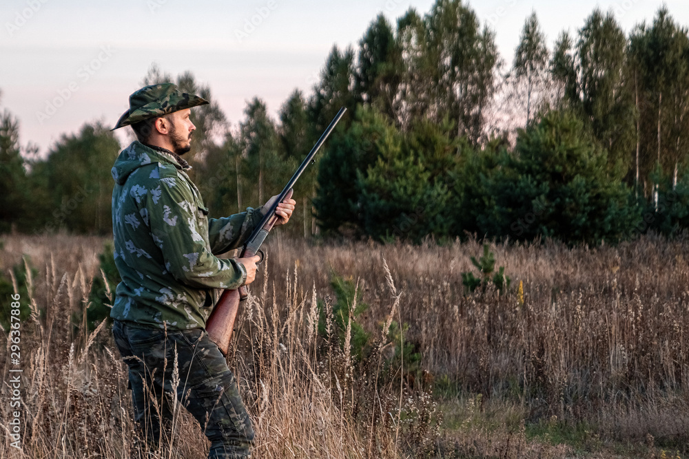 Hunter man in camouflage with a gun during the hunt in search of wild birds or game on the background of the autumn forest. Autumn hunting season. The concept of a hobby, killing. Hunter man in camouflage with a gun during the hunt in search of wild birds or game on the background of the autumn forest. Autumn hunting season. The concept of a hobby, killing.
