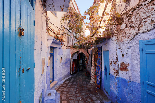 Narrow street of Chefchaouen blue city in Morocco with bright blue walls and hand made carpets hanging around.