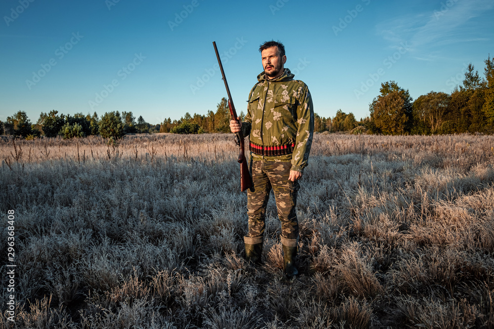 Hunter man in camouflage with a gun during the hunt in search of wild birds or game on the background of the autumn forest. Autumn hunting season. The concept of a hobby, killing. Hunter man in camouflage with a gun during the hunt in search of wild birds or game on the background of the autumn forest. Autumn hunting season. The concept of a hobby, killing.