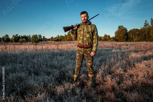 Hunter man in camouflage with a gun during the hunt in search of wild birds or game on the background of the autumn forest. Autumn hunting season. The concept of a hobby  killing.