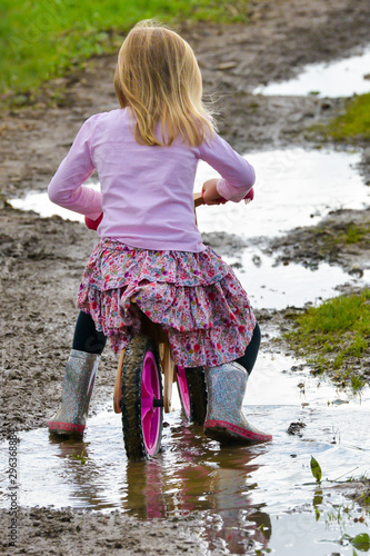 Canvas-taulu Rear view of young girl riding her bike through muddy  puddles