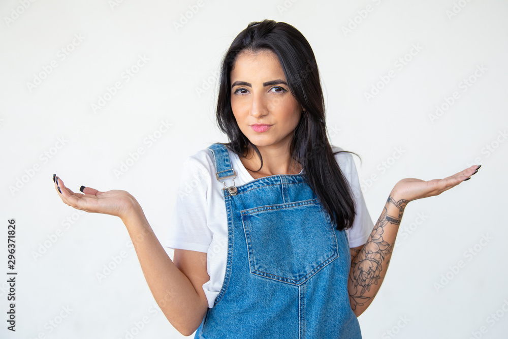 Doubting woman with raised hands looking at camera. Attractive brunette posing on light background. Concept of doubt Doubting woman with raised hands looking at camera. Attractive brunette posing on light background. Concept of doubt