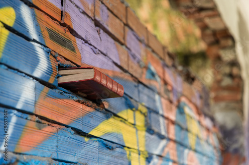 Libro rosso tra fessura in muro di mattoni con graffiti colorati photo