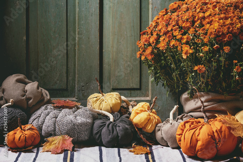 Wool and textile pumpkins for Halloween or Thanksgiving holidays home decor with autumn leaves, pot of chrysanthemums flowers on knitted doormat with old wooden door at background. photo