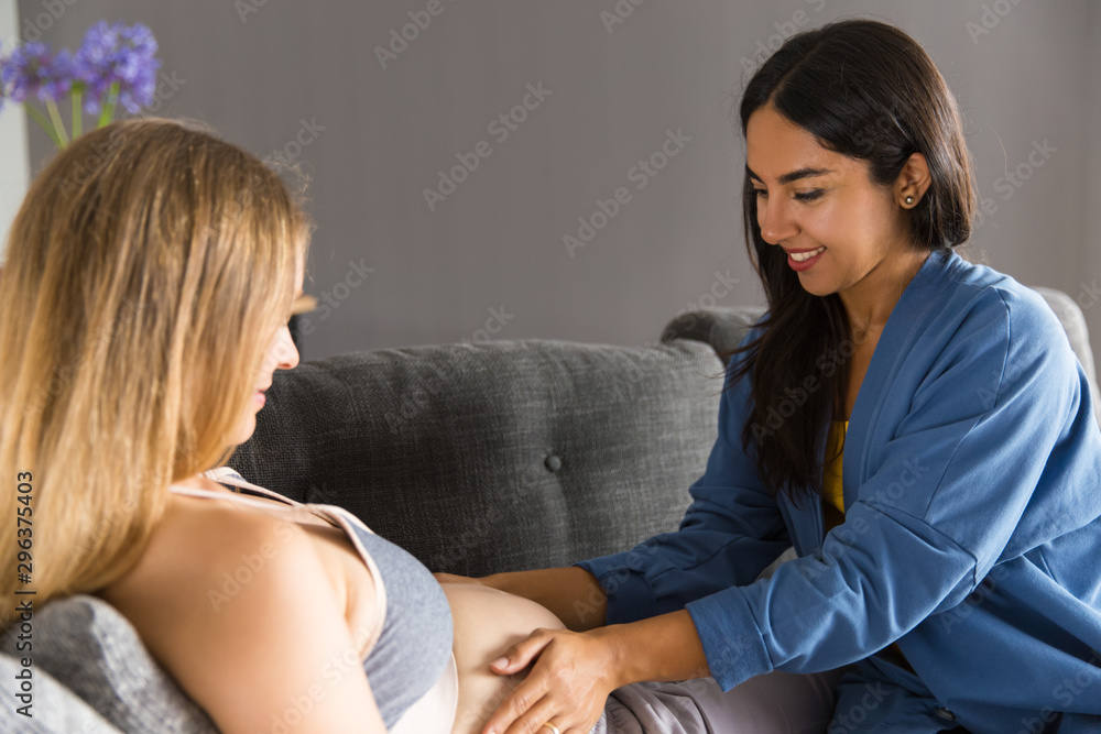 Midwife visiting expectant mother. Young woman touching belly of pregnant patient lying on couch. Prenatal care concept Midwife visiting expectant mother. Young woman touching belly of pregnant patient lying on couch. Prenatal care concept