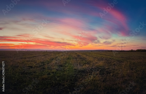 Majestic autumn sunset over a countryside open field. Soft and colorful clouds over empty plain land. © psychoshadow