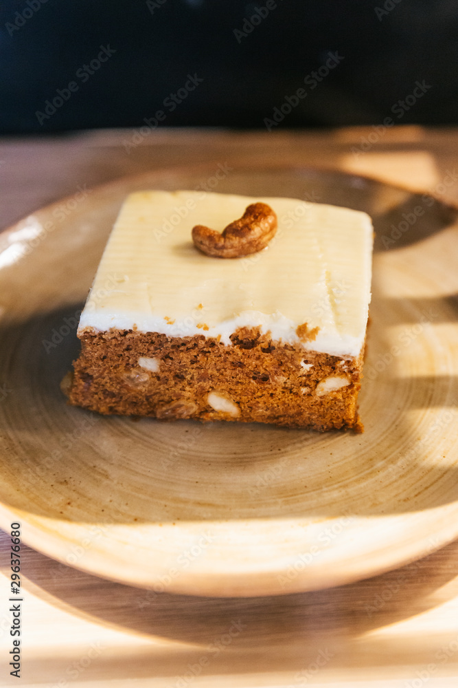 Almond coffee cake in square shape topping with white cream and cashew nut.