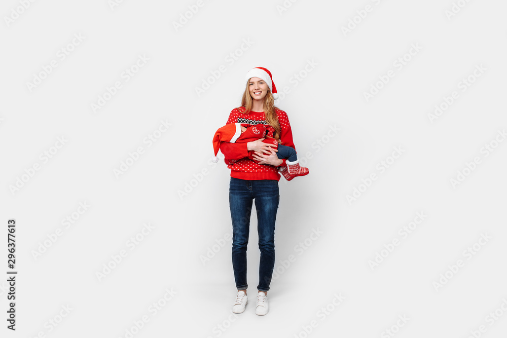Young mother in santa hat with little baby in santa costume standing on white background Young mother in santa hat with little baby in santa costume standing on white background