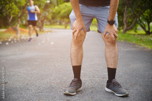 Male runner athlete knee injury and pain. Man suffering from painful knee while running in the public park. © Oranuch