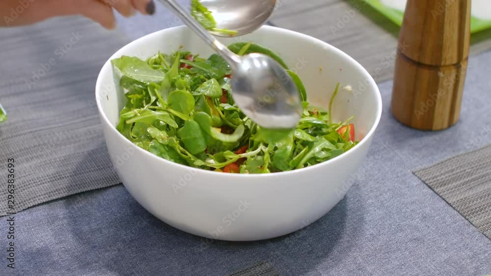 Woman mixing delicious superfood salad ingredients with spoons in kitchen Woman mixing delicious superfood salad ingredients with spoons in kitchen
