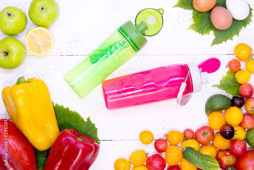 Smoothies with vegetables. Sports pink and green bottle on a white wood texture background top view around different vegetables. Sports nutrition and diet. The concept raw food detoxification.