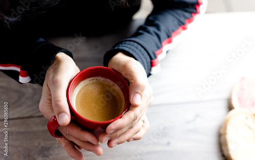 Top view of an unidentifiable person holding a red mug filled with coffee on a wooden rustic table