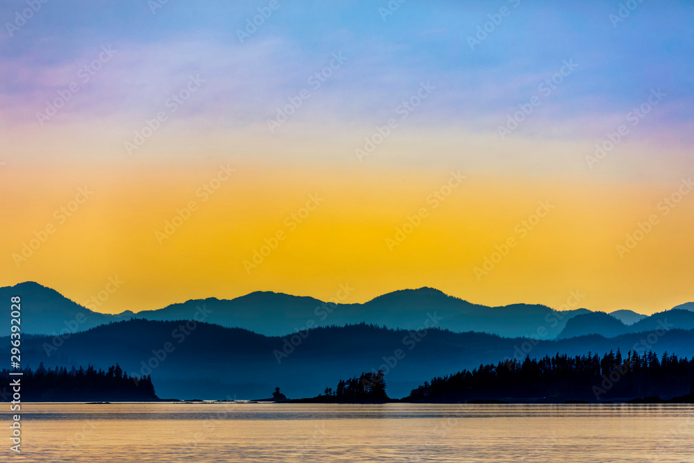 Fototapeta premium Yellow Sunset over Mountains, Ocean, Silhouetted
