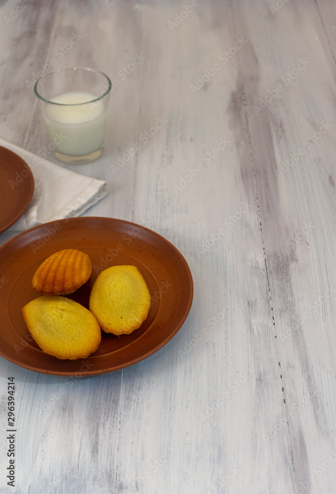 Madeleines and milk in wooden rustic background with copy space in portrait position Madeleines and milk in wooden rustic background with copy space in portrait position