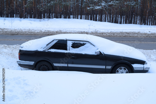 Black car near the road asphalt and snowy forest. Winter.