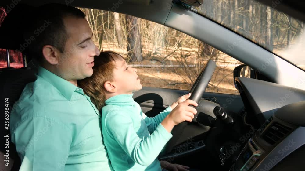 Happy child turns the wheel in the car. Father shows the device of the ...