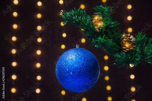 There is blue ball on the green xmas tree branch. There are glowing lights/bokeh and on the background. Merry Christmas. Happy New Year 2020. 