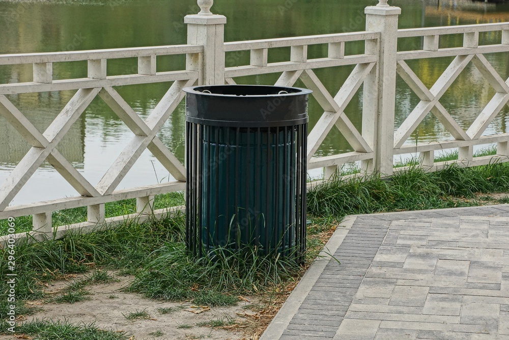 Obraz premium one black metal urn is standing by a white wooden fence on the shore near the water of a reservoir