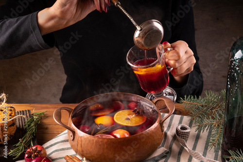 Female hands pour hot mulled wine from a copper pan into a glass.