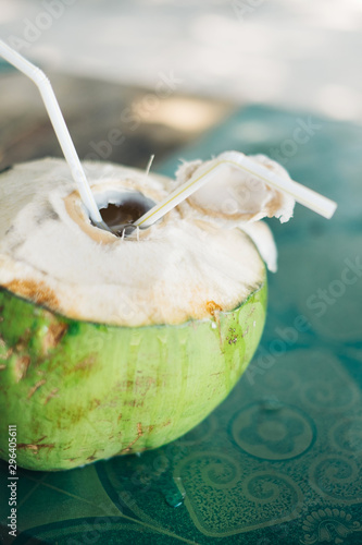 Opened green young  coconut with two plastic straws inserted for drinking the fresh water inside