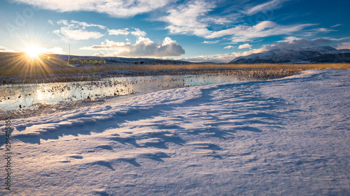 River flows through frozen field covered with snow