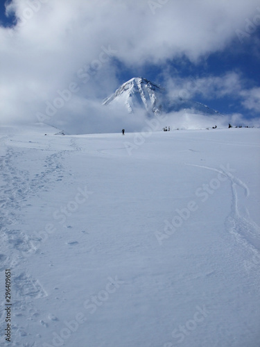 A lone skier in the distance makes his way up the snowfield on the Mt. Hood Cooper Spur route. Mt Hood above him is engulfed in clouds.